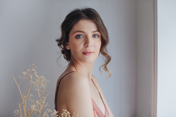 Portrait of beautiful tender young blue-eyed woman in silky nightgown looking at camera.