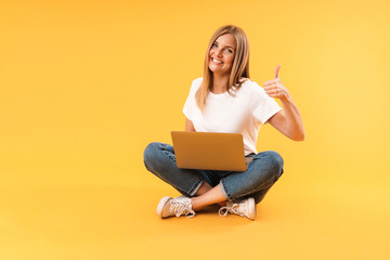 Image of caucasian blond woman showing thumb up and using laptop computer while sitting with legs...
