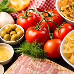 Italian food ingredients - pasta, vegetables, mushrooms, bacon, eggs, olives. Flat lay on dark wooden background