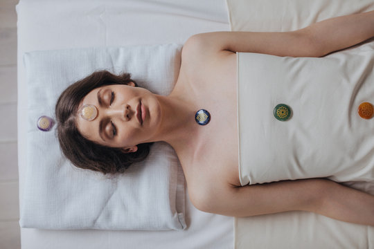 From above photo of pretty woman lying on massage table with chakra crystals on her body.
