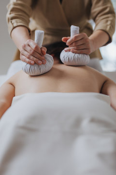 Unrecognisable woman masseuse using herbal compress for back massaging.