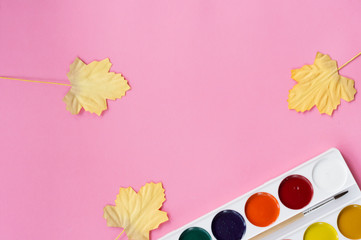 on a pink background, yellow leaves and paint with tassels, top view