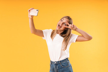 Image of attractive blond woman showing peace fingers while taking selfie photo on smartphone