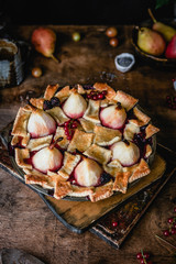 pear pie with berries on wooden boards among fresh currants, flowers and fresh pears on brown wooden background
