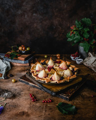 pear pie with berries on wooden boards among fresh currants, flowers and fresh pears on brown wooden background
