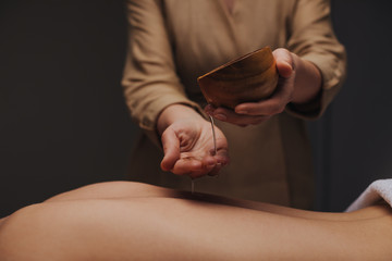Hands of unrecognisable woman masseuse pouring massage oil over woman's back.