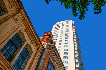 old and new - old brick house on a background of a white skyscraper on a background of clear blue...