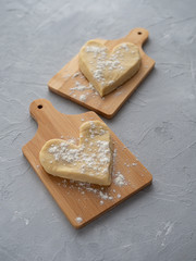 Two heart-shaped muffin blanks on small wooden planks against a gray concrete background.