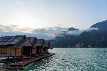 Obraz premium Raft houses at sunrise with clouds above water and mountain