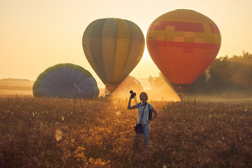 Obraz premium Balloons getting ready to take off on the field in the fog and female photographer at dawn.