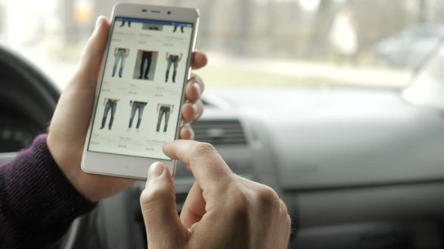 A man looks at the goods in the online clothing store, sitting in the car. Smart phone online shopping.