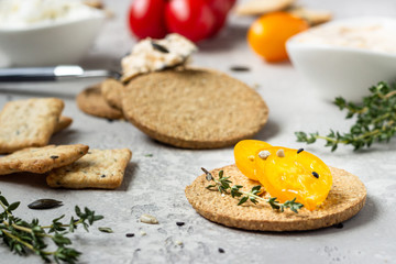Thin crispy wholegrain crackers with cream cheese and tomatoes on a black plate. 