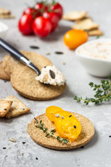 Thin crispy wholegrain crackers with cream cheese and tomatoes on a black plate. 