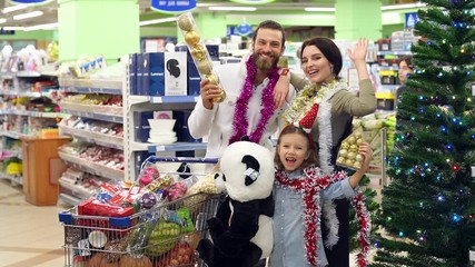 Portrait of a happy family in the supermarket before christmas. A happy family with a child buys groceries, Christmas decorations, and presents for Christmas or New Year in a large supermarket.