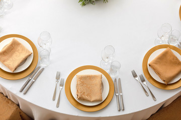 Top view of elegant plates with folded napkins and glassware served on clean white cloth in...