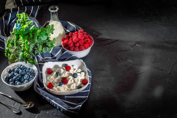 Cottage cheese with fresh raspberries and blueberries in a bowl for healthy breakfast on dark background