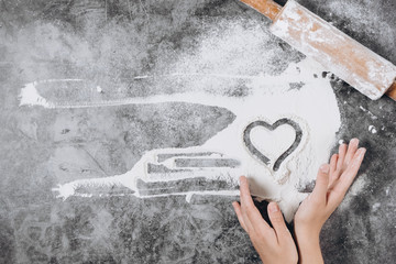 Baking background. Girl hands keep rolling pin and heart of flour on gray table with copy space, top view. Valentine's Day