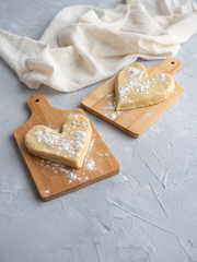 Two heart-shaped buns on small wooden planks on a gray concrete background with a cloth napkin.