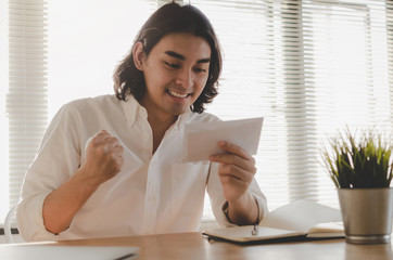 happy young asian employee business man holding money bonus card in paper envelope to increasing of salary or promotion new position in office, new job celebrate salary and resignation letter concept