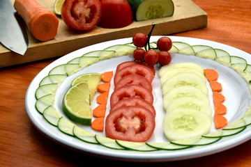 tomato salad, cucumber, carrot, accompanied with a lemon, placed on a white plate on a wooden table and with background the inputs used