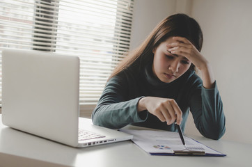 tired and frustrated stressed asian young employee business woman working finance about cost with laptop computer and document report on desk at home office, financial crisis and marketing concept