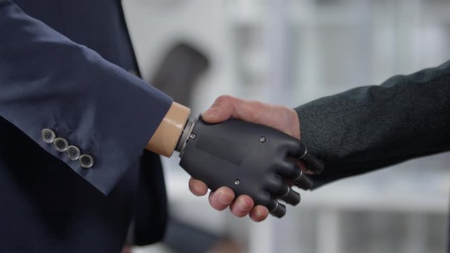 Close up shot of businessman with prosthetic hand giving handshake to make colleague in the office