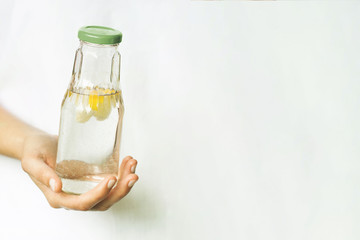 Glass bottle with water and slices of lemon in a female hand. The topic of the importance of drinking your daily fluid intake. Healthy lifestyle, zero waste, plastic-free, eco-friendly shopping, vegan