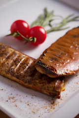 Grilled mackerel fish fillet in tomato mustard sauce, served with cherry tomatoes, rosemary and lemon on white plate, wooden table