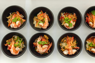 Top view of rows of seafood snack with shrimp in small black bowls on white background