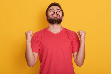 Fototapeta premium Image of happy positive excited young male clenching fists and screaming, wearing red casual t shirt, having good news, celebrating his victory or success, wins lottery. People emotions concept.