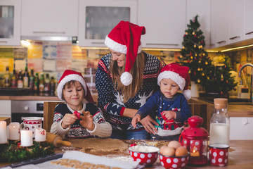 Sweet toddler child and his older brother, boys, helping mommy preparing Christmas cookies at home