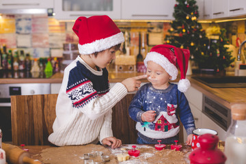 Sweet toddler child and his older brother, boys, helping mommy preparing Christmas cookies at home