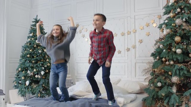Two smiling teens jumping bed in luxury house. Cheerful kids having jump party