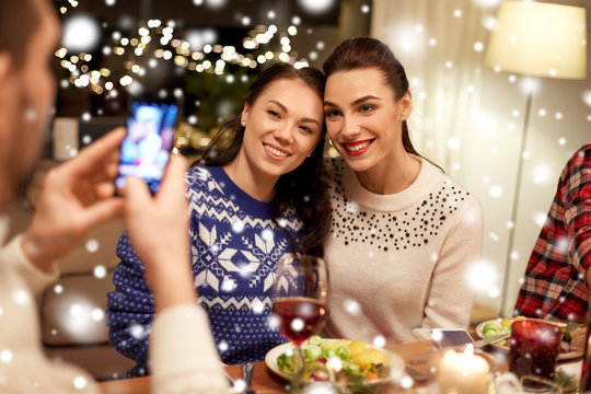 holidays and celebration concept - happy friends having christmas dinner at home and taking picture by smartphone over snow