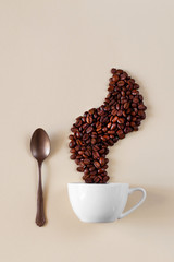 Creative coffee still life. Coffee beans are laid out over the cup in the form of steam. A spoon...