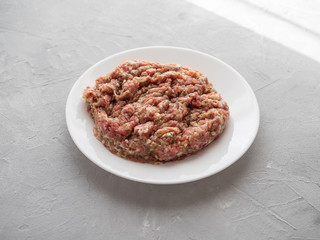 Meat natural minced pork, lamb, beef on a white plate on a gray concrete background.
