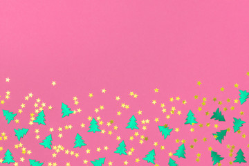 Green metallic foil christmas trees and gold stars confetti sparse on pink background. Simple holiday concept. Design template. Frame with copy space. Winter festive backdrop. Top view, flat lay.