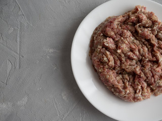 Meat natural minced pork, lamb, beef on a white plate on a gray concrete background.