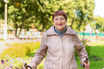 An elderly woman walks nordic with sticks in the Park on a Sunny summer day outdoors