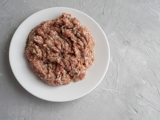 Meat natural minced pork, lamb, beef on a white plate on a gray concrete background.