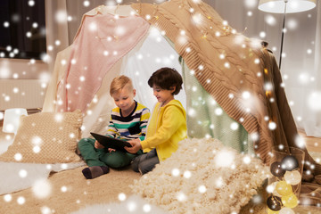 Obraz na płótnie Canvas childhood, technology and hygge concept - happy little boys with tablet pc computer in kids tent at home over snow