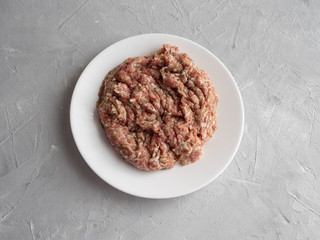 Meat natural minced pork, lamb, beef on a white plate on a gray concrete background.