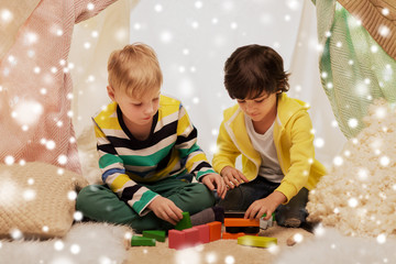 childhood, christmas and friendship concept - happy boys playing toy blocks in kids tent or teepee...