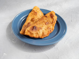 Delicious fresh pasties stuffed with meat for the blue plate, grey concrete background.
