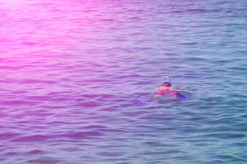A man in a mask and snorkel diving into the sea wave.