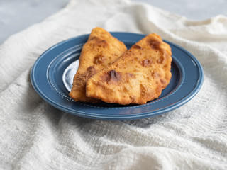 Delicious fresh pasties stuffed with meat for the blue plate, grey concrete background.