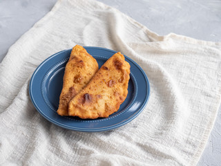 Delicious fresh pasties stuffed with meat for the blue plate, grey concrete background.