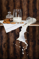 The poured milk fallen from the top shelf with cookes on a wooden background