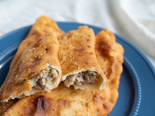 Delicious fresh pasties stuffed with meat for the blue plate, grey concrete background.