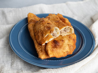 Delicious fresh pasties stuffed with meat for the blue plate, grey concrete background.